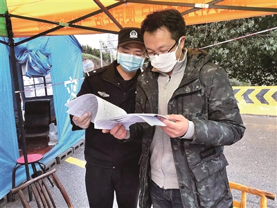 圖為疫情期間，謝睿（右）在咸豐縣清坪鎮(zhèn)把界村大河邊交通卡點(diǎn)查看車(chē)輛出入登記臺(tái)賬。 （湖北省咸豐縣紀(jì)委監(jiān)委供圖）